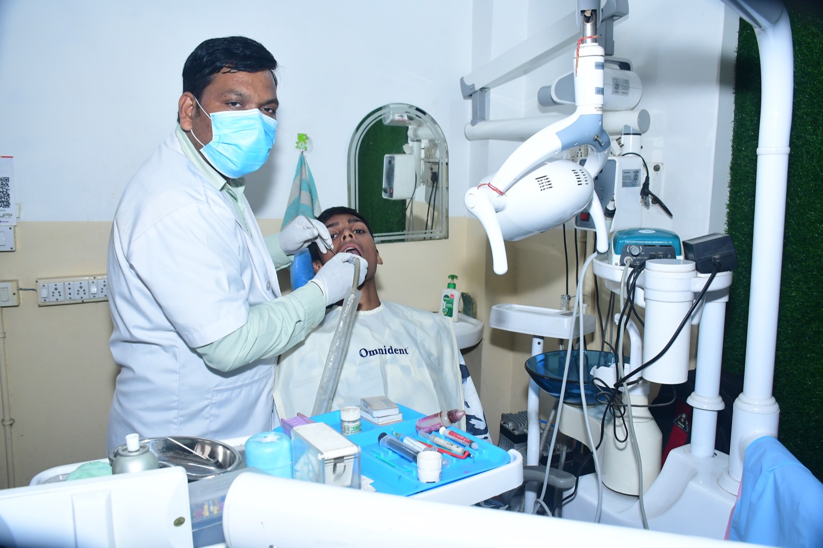 Modern dental exam room with dental chair, overhead light, monitors, and dental equipment.